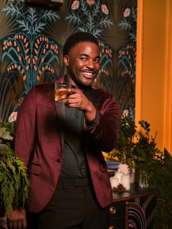 Man in a burgundy suit holding a drink at a party