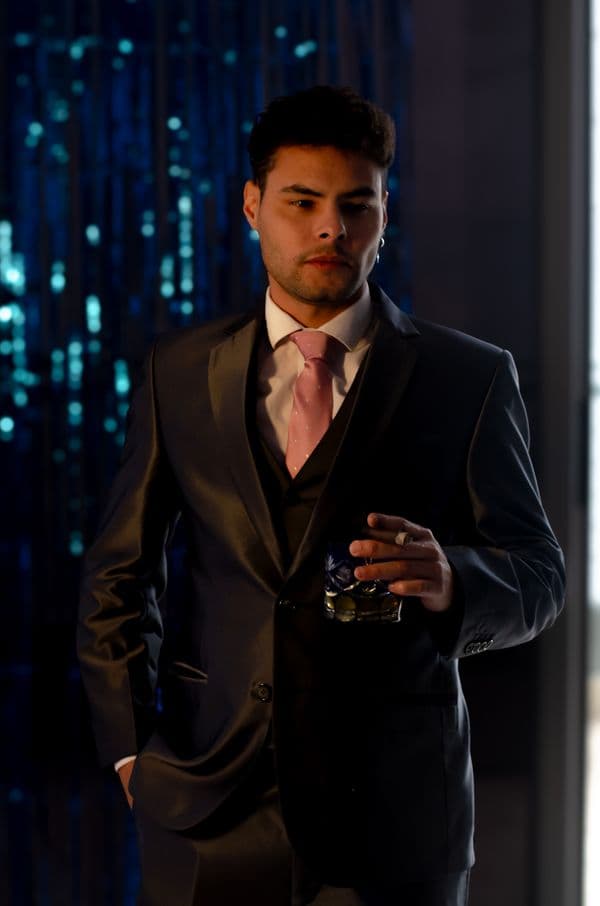Man in a dark suit holding a drink indoors